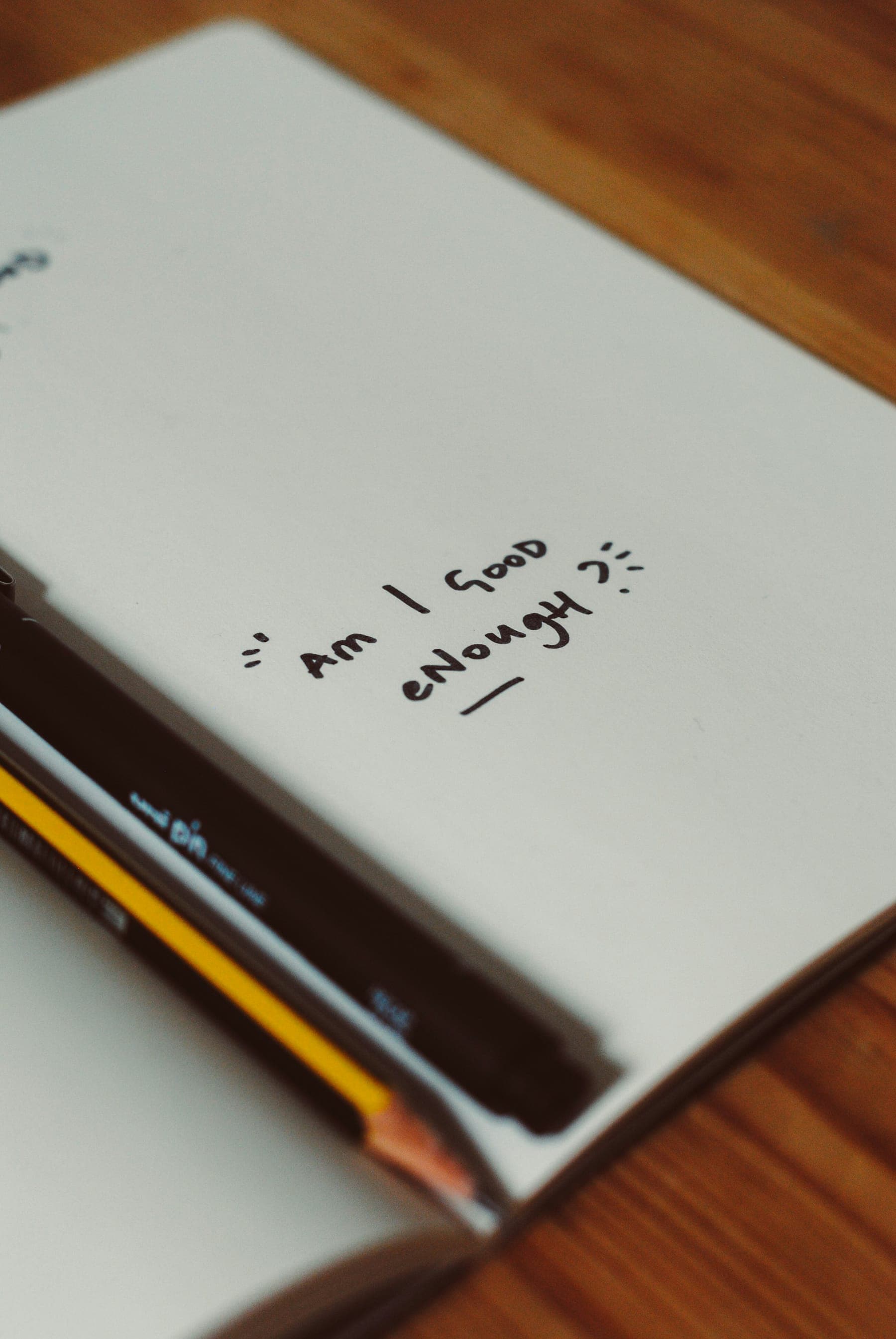 A notebook page with the handwritten question “Am I good enough?” beside a pencil
